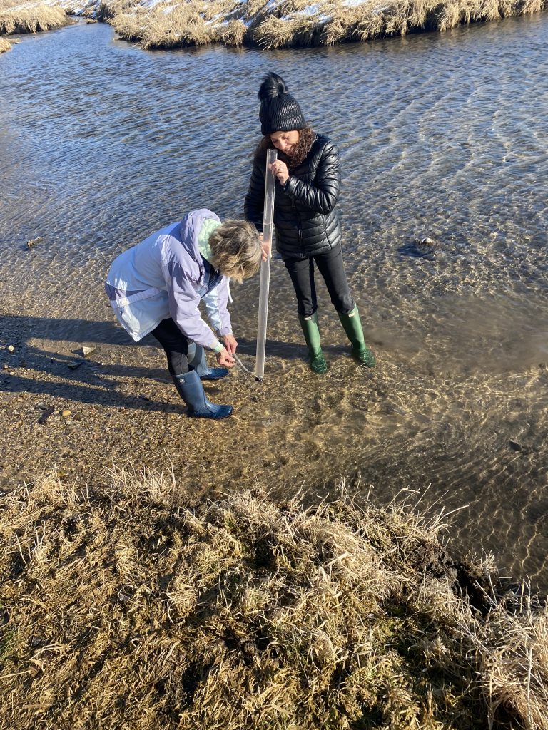 Barb and Paula stand in the stream and look down a transparency tub to measure water clarity.
