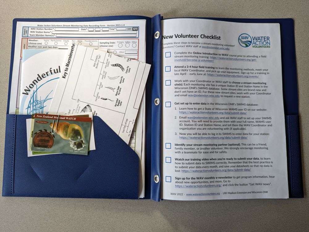 A blue folder is open on a table. In side the folder is a "New Volunteer Checklist", and a variety of paper resources tucked into the left pocket.