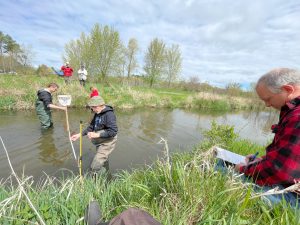 Group of volunteers stand in a stream with a net and measuring tape. They are measuring the width of the river. 