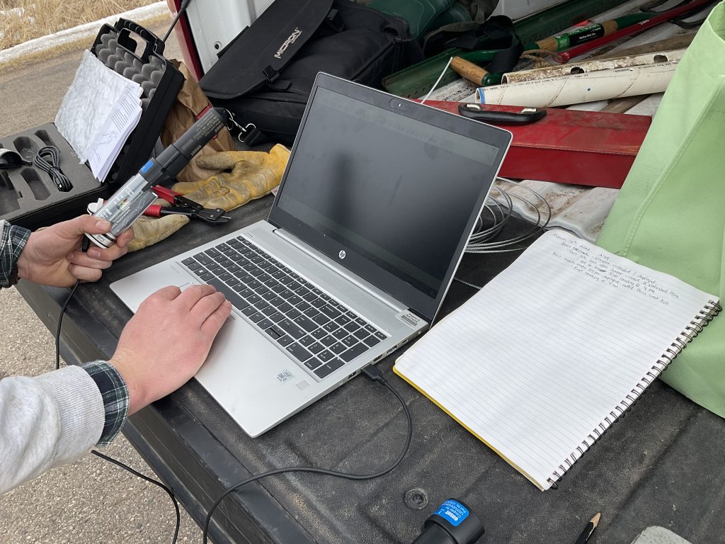 Laptop with a thermistor attached to it. Next to the laptop sits a notebook with data written on it. 