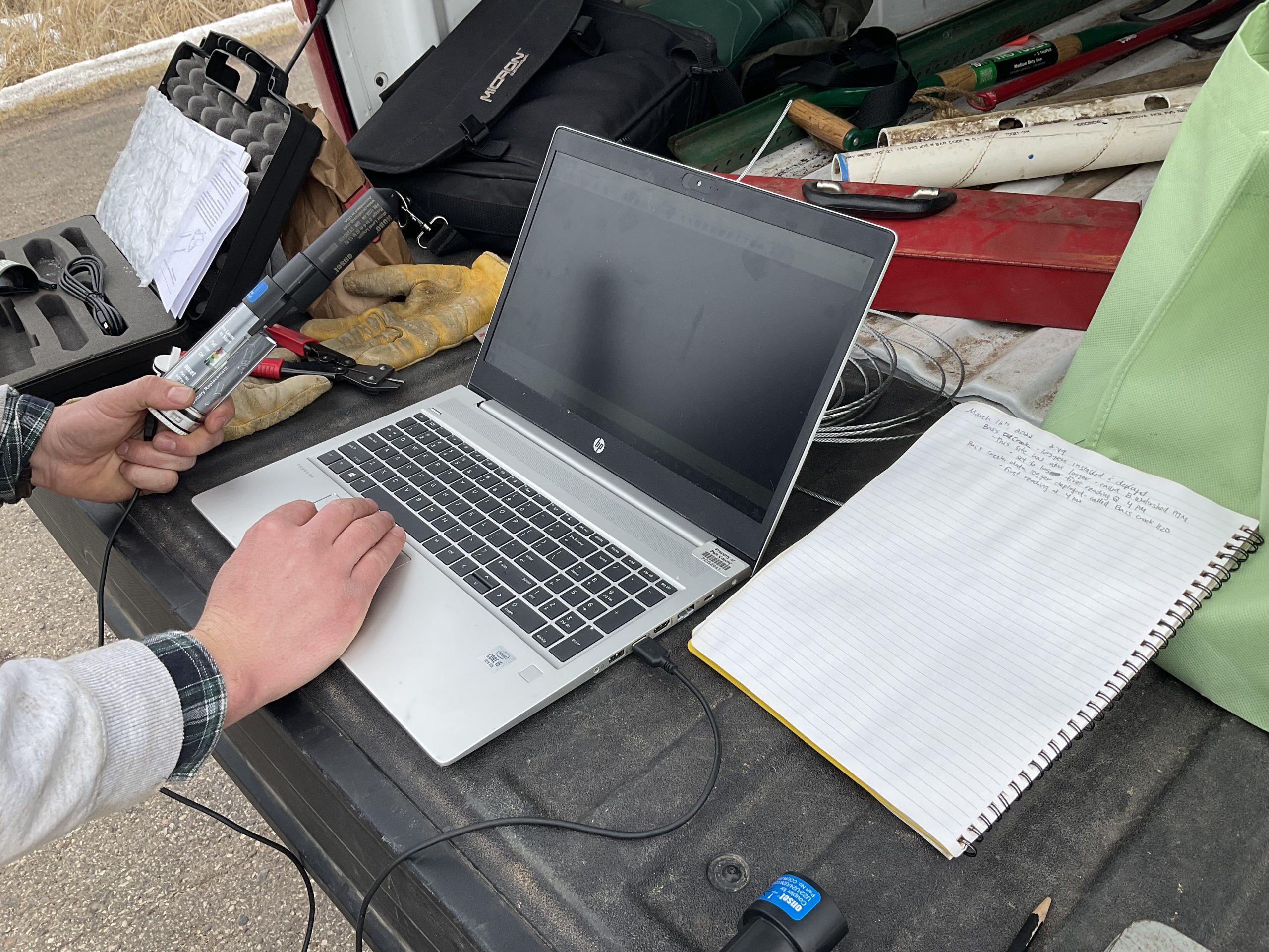 Laptop with a thermistor attached to it. Next to the laptop sits a notebook with data written on it. 