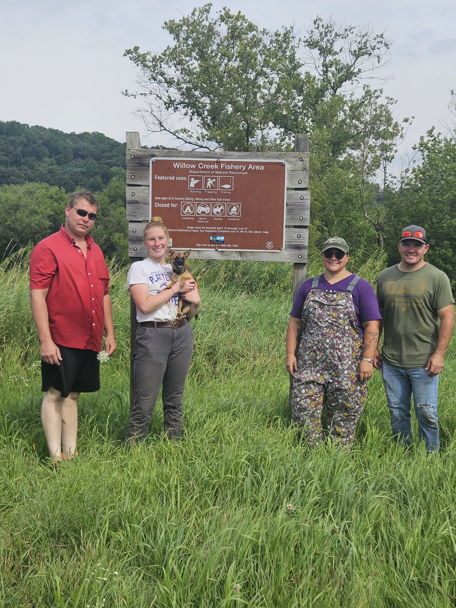 Four volunteers stand in a field in front of a brown sign. 