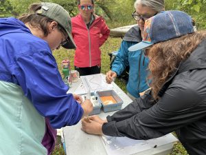 A group of volunteers measure dissolved oxygen outside. Their materials are on a white table. 
