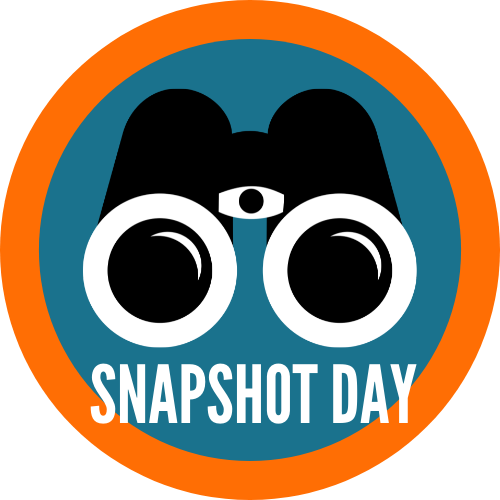 black binoculars in a blue circle. The circle has a thick orange border. Text at the bottom reads Snapshot Day.